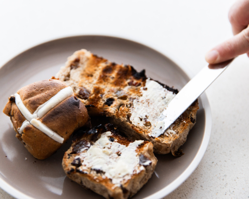 spreading butter on a freshly toasted hot cross bun - Australian Stock Image