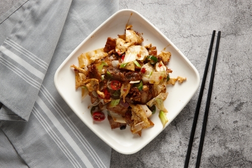 Stir fried pork slices with vegetables with black chopsticks resting on the surface counter - Australian Stock Image