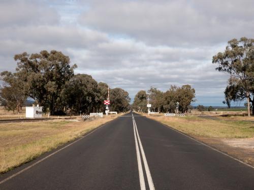 Straight bitumen road with double white lines and level crossing - Australian Stock Image