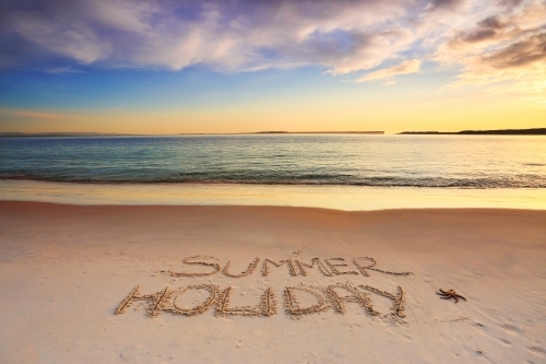 Summer holiday etched into the sand on the shoreline of a beach with early morning light. - Australian Stock Image