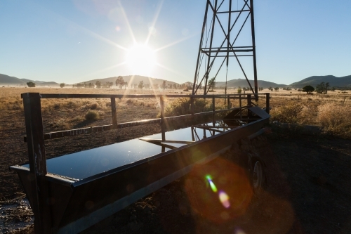 Sun flare over water trough on farm with windmill - Australian Stock Image