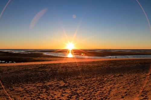 Sun rising through blue sky over ocean channel and sandy coastline - Australian Stock Image