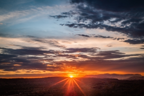 Sun setting in cloudy sky over rural landscape - Australian Stock Image