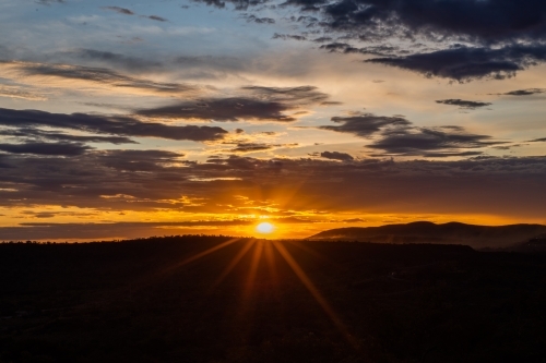 Sun setting in cloudy sky over rural landscape - Australian Stock Image