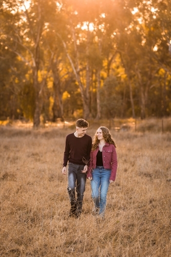 Sun shining on two youth walking through paddock with trees in background - Australian Stock Image