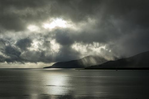 Sun shining through the clouds onto ocean and mountain - Australian Stock Image