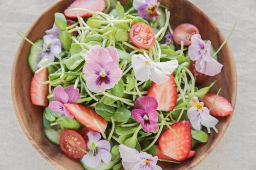 Sunflower sprouts, cucumber and edible flowers salad on wooden bowl - Australian Stock Image