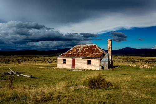 Sunlight and storms at an old hut in Snowy Mountains, Kosciuszko National Park - Australian Stock Image