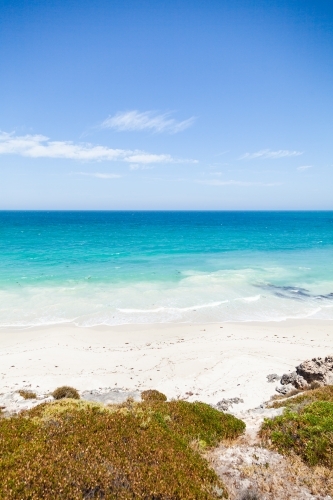 Sunlit coastland with view of shrubs, beach and clear blue coastal waters - Australian Stock Image