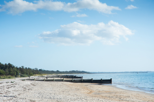 Sunny beach with groynes, blue sky and ocean - Australian Stock Image