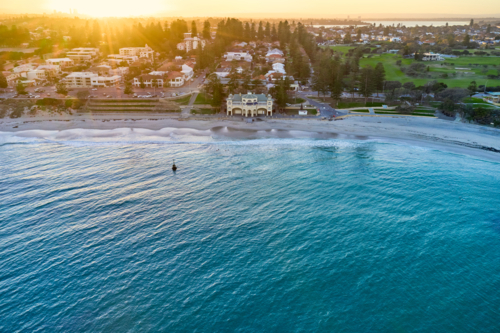 Sunrise over Perth's renowned Cottesloe beach, with the silhouette of the CBD skyline on the horizon - Australian Stock Image