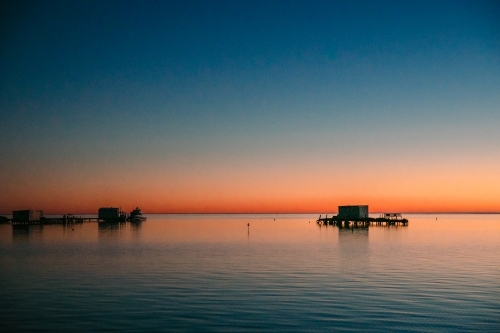 Sunrise over the calm ocean with jetties and fishing shacks - Australian Stock Image