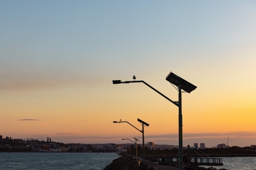 Sunset at the Stockton beach breakwall with seagulls sitting on light poles - Australian Stock Image
