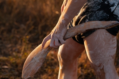 Sunset light on First Nations digging stick held in hand of young person in ochre body paint - Australian Stock Image