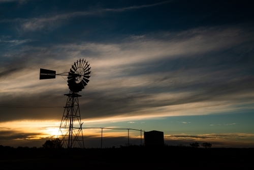 Sunset with windmill and water tank in the outback - Australian Stock Image