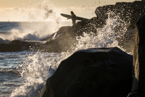 surfer on the rocks with crashing waves