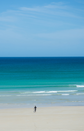 Surfer walking into water on turquoise beach - Australian Stock Image