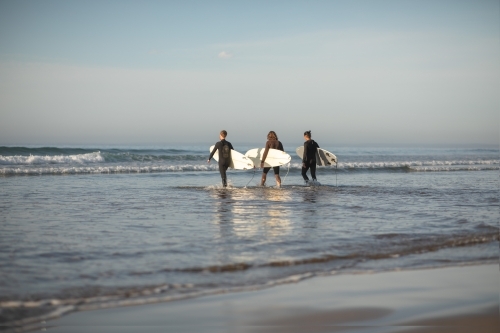 Surfers in distance running towards waves - Australian Stock Image