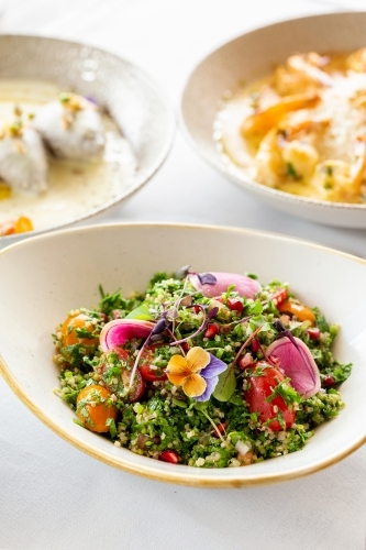 Tabouli quinoa salad topped with edible flowers and red radish. - Australian Stock Image