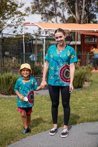 Teacher holding hand on young Aboriginal boy at preschool - Australian Stock Image