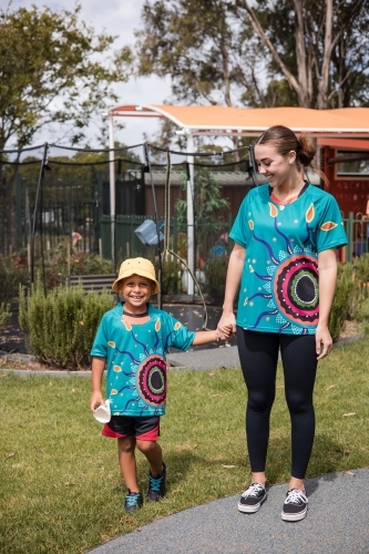 Teacher holding hand on young Aboriginal boy at preschool - Australian Stock Image