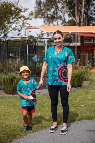 Teacher holding hand on young Aboriginal boy at preschool - Australian Stock Image