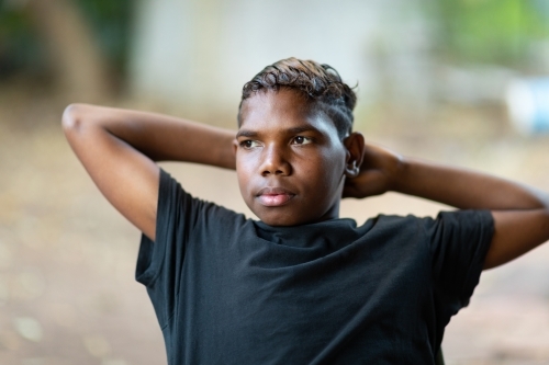 teen boy in black leaning back with arms behind his head