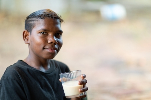 teen boy in black tee holding milk drink in glass looking at camera