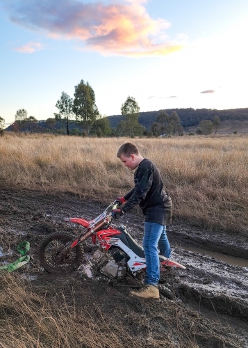 Teen boy on farm with motorbike stuck in the mud - Australian Stock Image