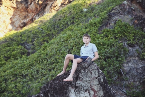 Teen boy sitting alone on rock - Australian Stock Image