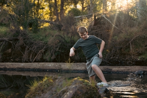 Teen boy walking through shallow creek on nature walk - Australian Stock Image