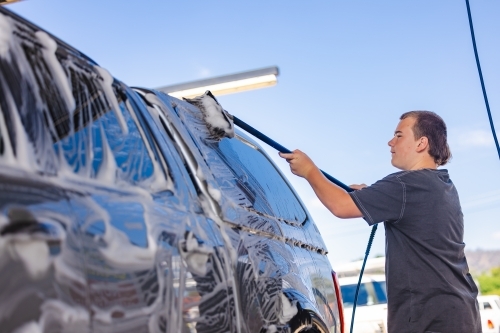 Teen boy washing vehicle in self-service car wash bay - Australian Stock Image