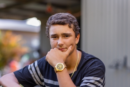 teen boy wearing watched looking at camera with hand on chin - Australian Stock Image