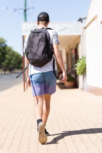 Teen boy with a backpack walking away on a footpath - Australian Stock Image