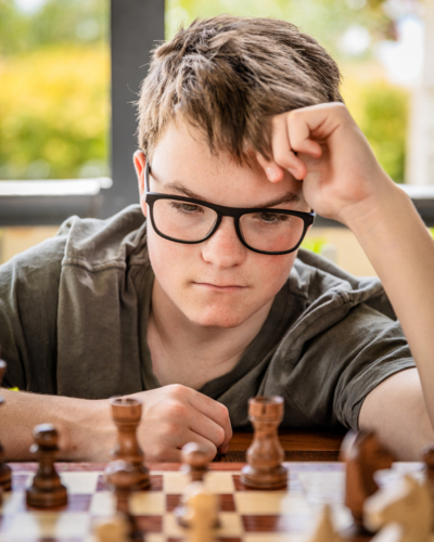 Teen boy with glasses contemplating a chess board - Australian Stock Image