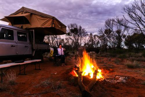 Teen girl sits by the fire at dusk in camp set up in outback Northern Territory