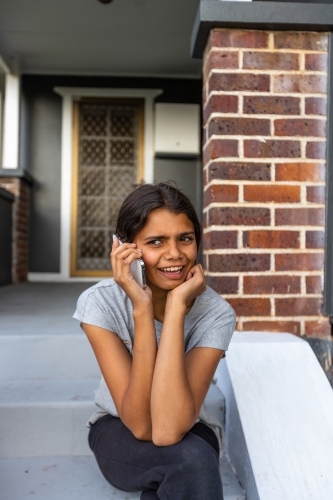 teen girl sitting on step holding mobile phone to her ear - Australian Stock Image