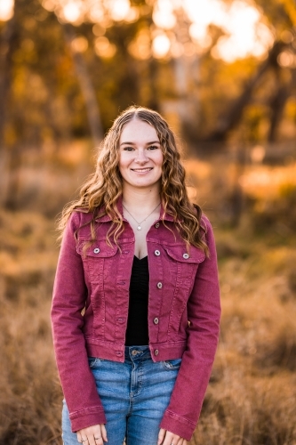 Teen girl standing in paddock in late afternoon light smiling portrait - Australian Stock Image