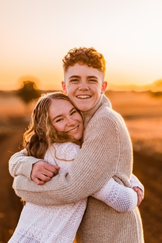 Teenage boy and girl hugging against sunset rural landscape - Australian Stock Image