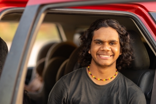 teenage boy in car smiling and looking at the camera from back seat with door open - Australian Stock Image