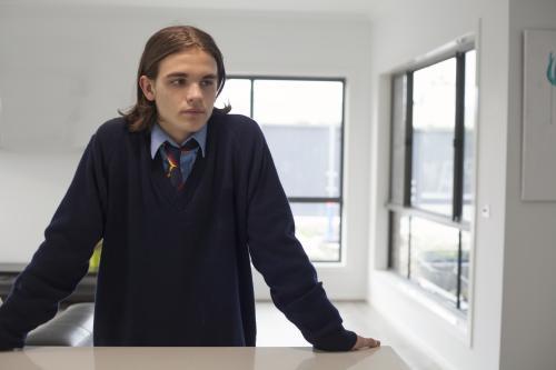 Teenage boy in high school uniform leaning on a bench at home - Australian Stock Image