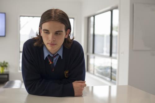 Teenage boy in high school uniform leaning on a bench at home - Australian Stock Image