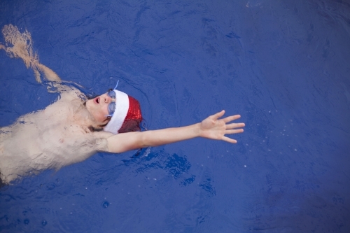 Teenage boy in Santa hat celebrating christmas in a pool - Australian Stock Image