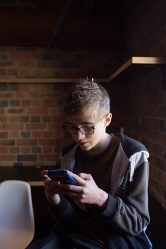 Teenage boy playing on mobile device - Australian Stock Image