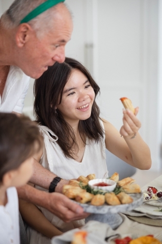 Teenage girl at table holding pastry with grandfather and brother - Australian Stock Image