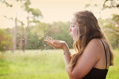 Teenage girl blowing confetti in a field - Australian Stock Image