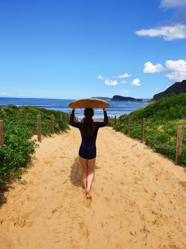 Teenage girl carrying a surfboard to the beach - Australian Stock Image