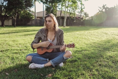 teenage girl playing ukulele in the park - Australian Stock Image