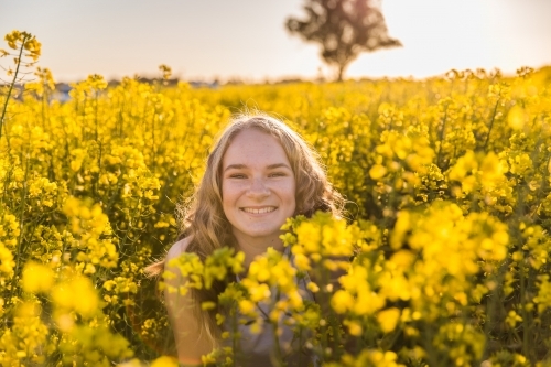 Teenage girl smiling among canola crop on farm - Australian Stock Image