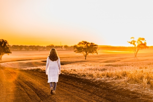 Teenage girl walking away from the camera on dirt road - Australian Stock Image